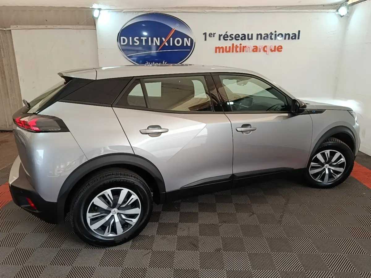 Vue de profil droit du Peugeot E-2008 électrique Active Pack gris clair, avec jantes distinctives et toit noir contrastant.