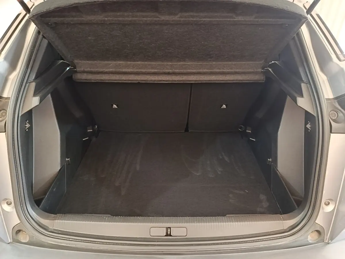 Coffre ouvert vu de l'arrière d'un Peugeot E-2008 électrique gris clair, montrant l'espace de chargement vide.