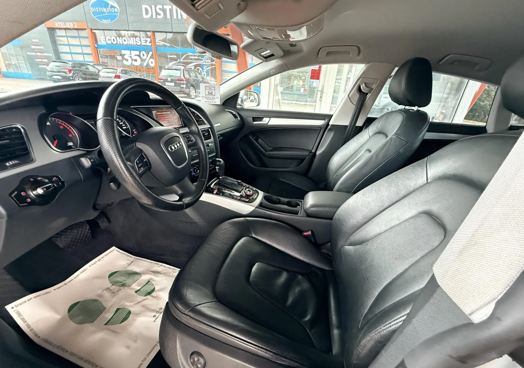 Intérieur de l'Audi A5 gris, vue côté conducteur montrant les sièges en cuir noir et le tableau de bord moderne.