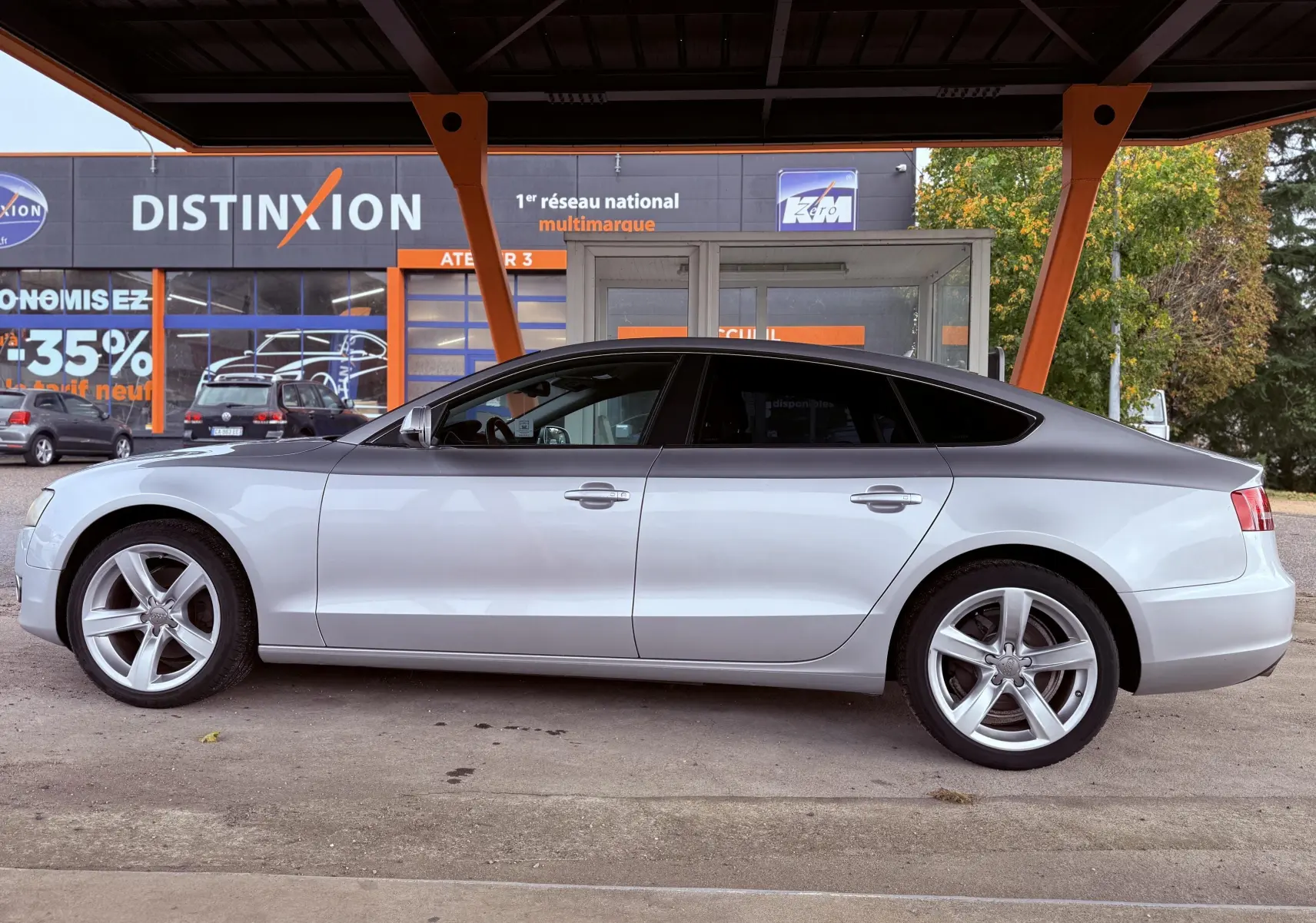 Profil côté gauche d'une Audi A5 gris clair 5 portes garée sous un abri avec jantes alliage 5 branches.