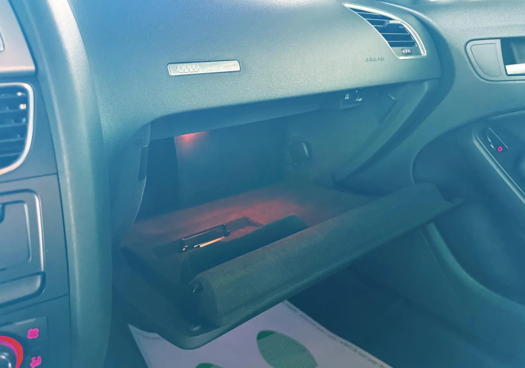 Gros plan sur la boîte à gants ouverte côté passager de l'Audi A5 gris, montrant l'intérieur éclairé et le tableau de bord noir.