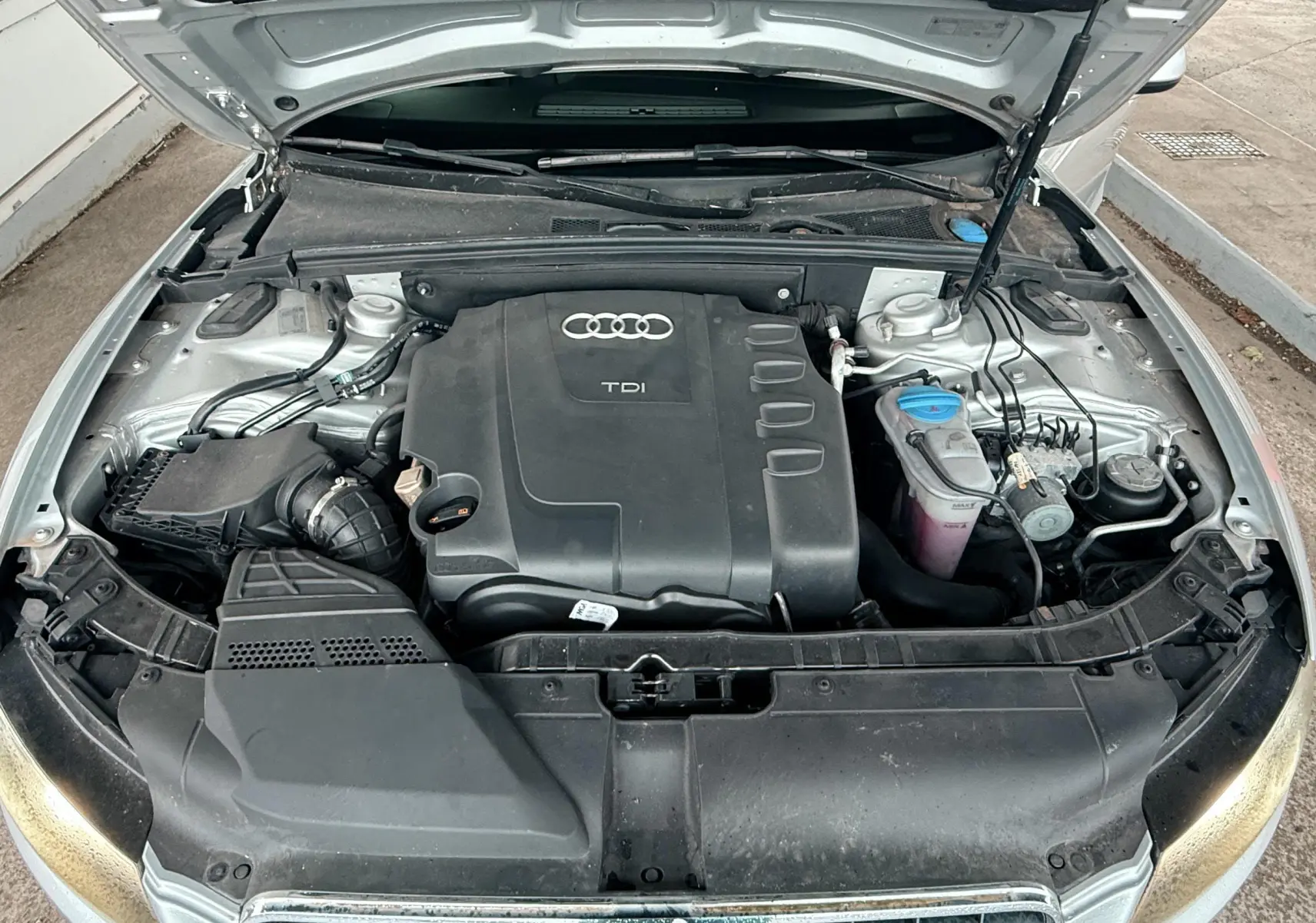 Vue plongeante sur le moteur TDI d'une Audi A5 gris avec capot ouvert montrant les composants sous le capot.
