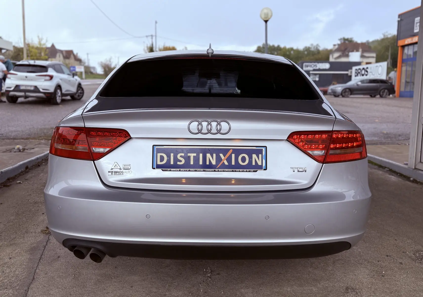 Vue arrière d'une Audi A5 gris métallisé avec feux rouges allumés et double sortie d'échappement visible.