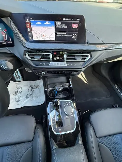 Vue intérieure centrée sur la console centrale et l'écran tactile de la BMW Série 1 118d Edition Sport gris foncé, avec volant cuir et commandes multifonctions.