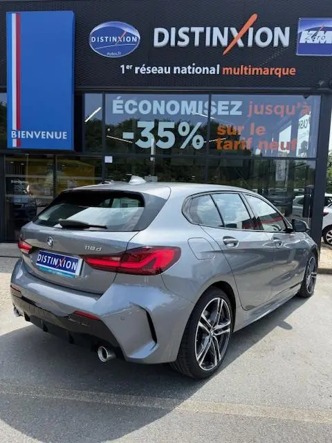 BMW Série 1 118d gris foncé vue 3/4 arrière droite devant une concession Distinxion.