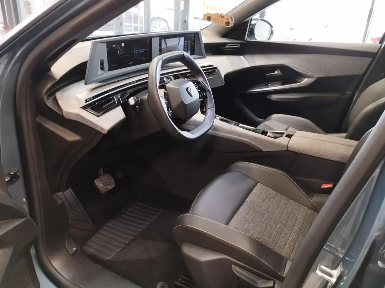 Vue intérieure côté conducteur du Peugeot 5008 2025 avec sellerie tissu gris et noir, volant compact et double écran HD flottant.