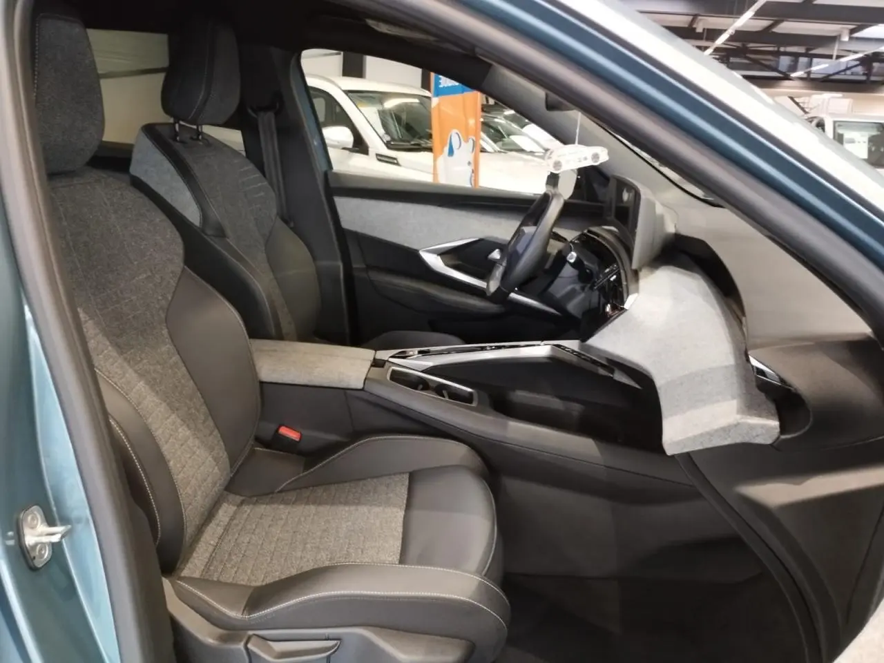 Intérieur avant droit du Peugeot 5008 bleu Ingaro 2025, sièges tissu et cuir, planche de bord avec décor tissu clair.