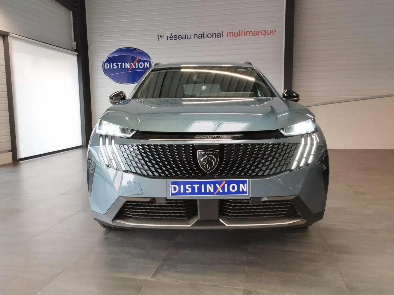 Vue de face du Peugeot 5008 2025 bleu Ingaro avec calandre noire et feux LED à griffes allumés.