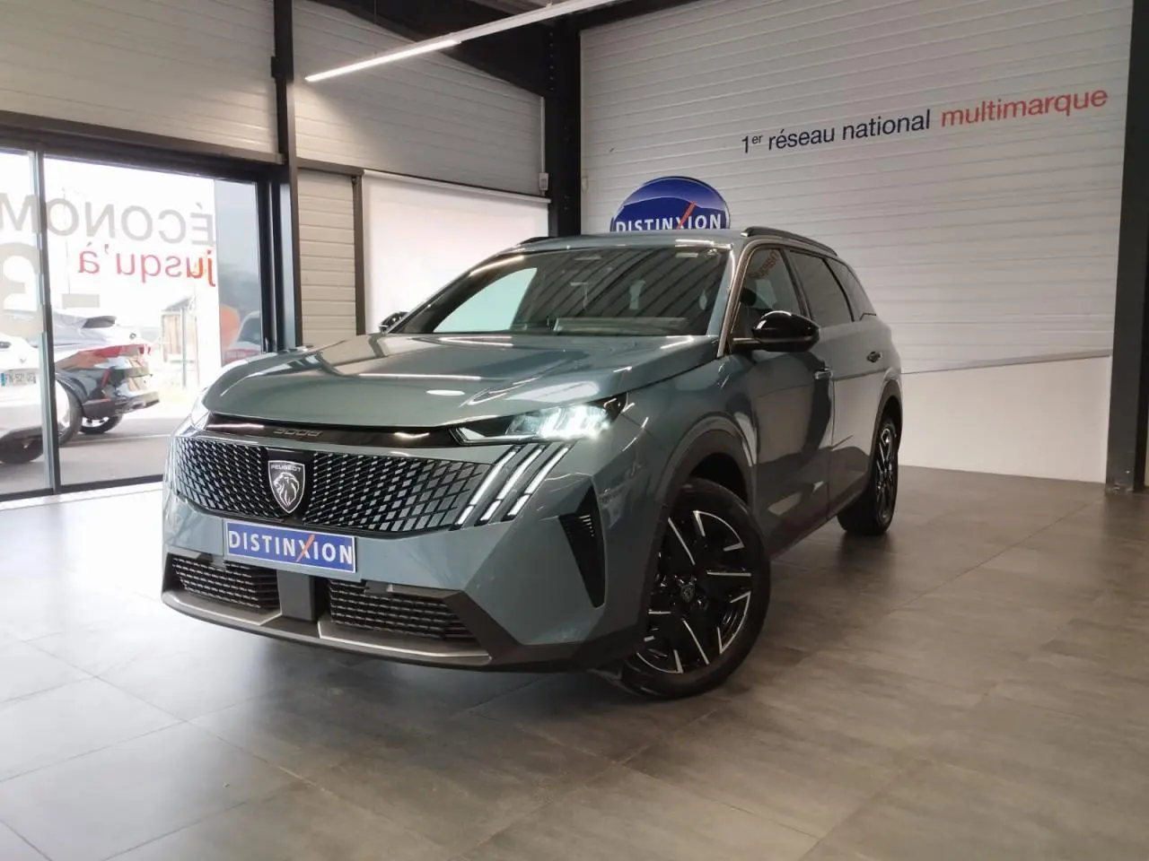 Peugeot 5008 bleu Ingaro vue 3/4 avant droit en intérieur avec calandre noire et jantes alliage noires.