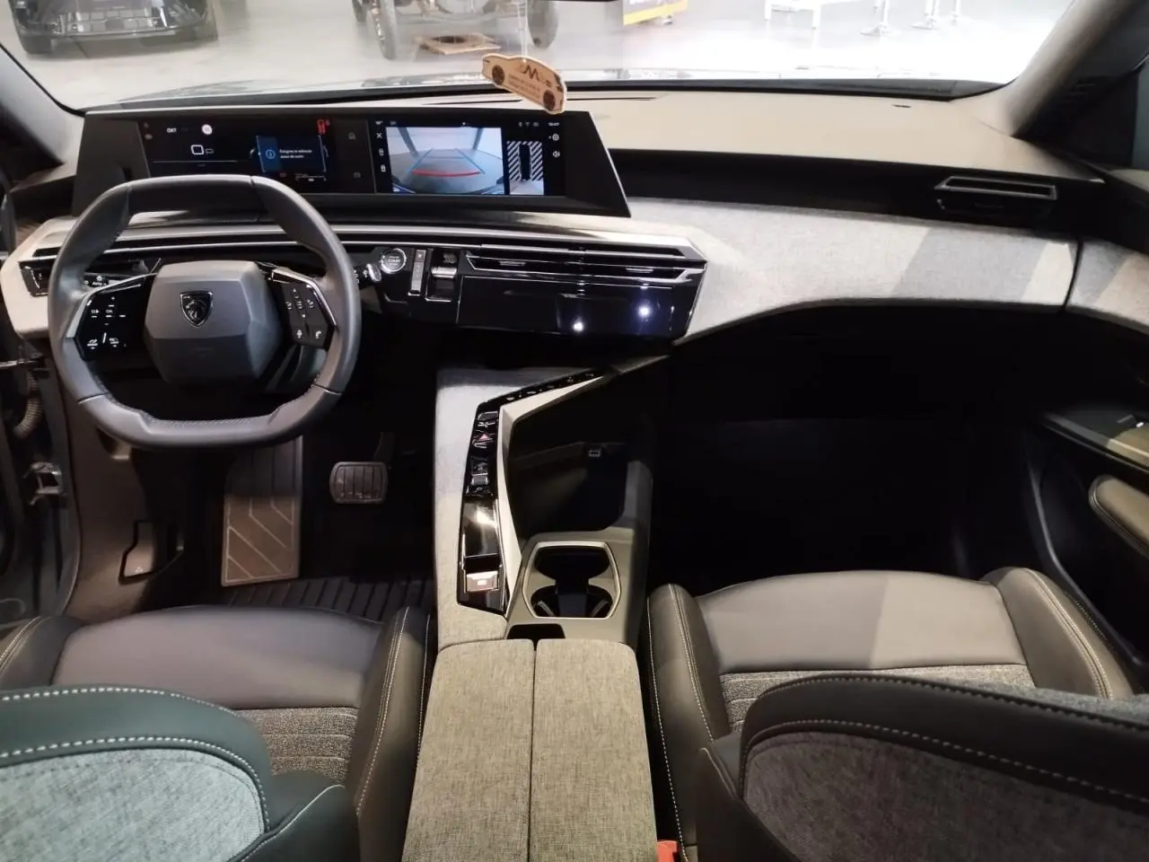 Vue intérieure avant du Peugeot 5008 2025 avec tableau de bord noir et tissu gris, volant compact et double écran HD flottant.