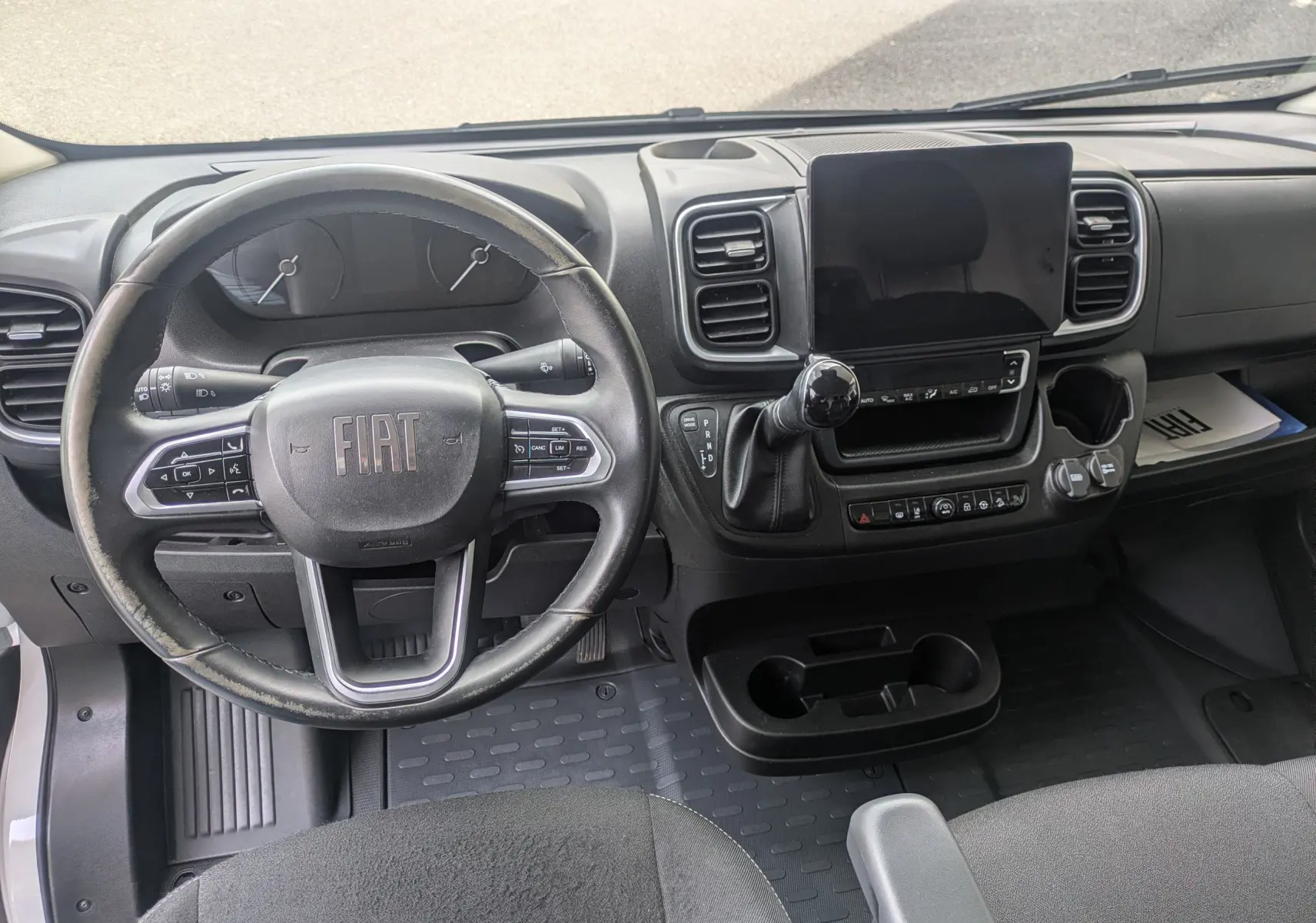 Vue intérieure du tableau de bord du Fiat Ducato Fourgon 2025, avec volant noir, écran tactile central et levier de vitesse.