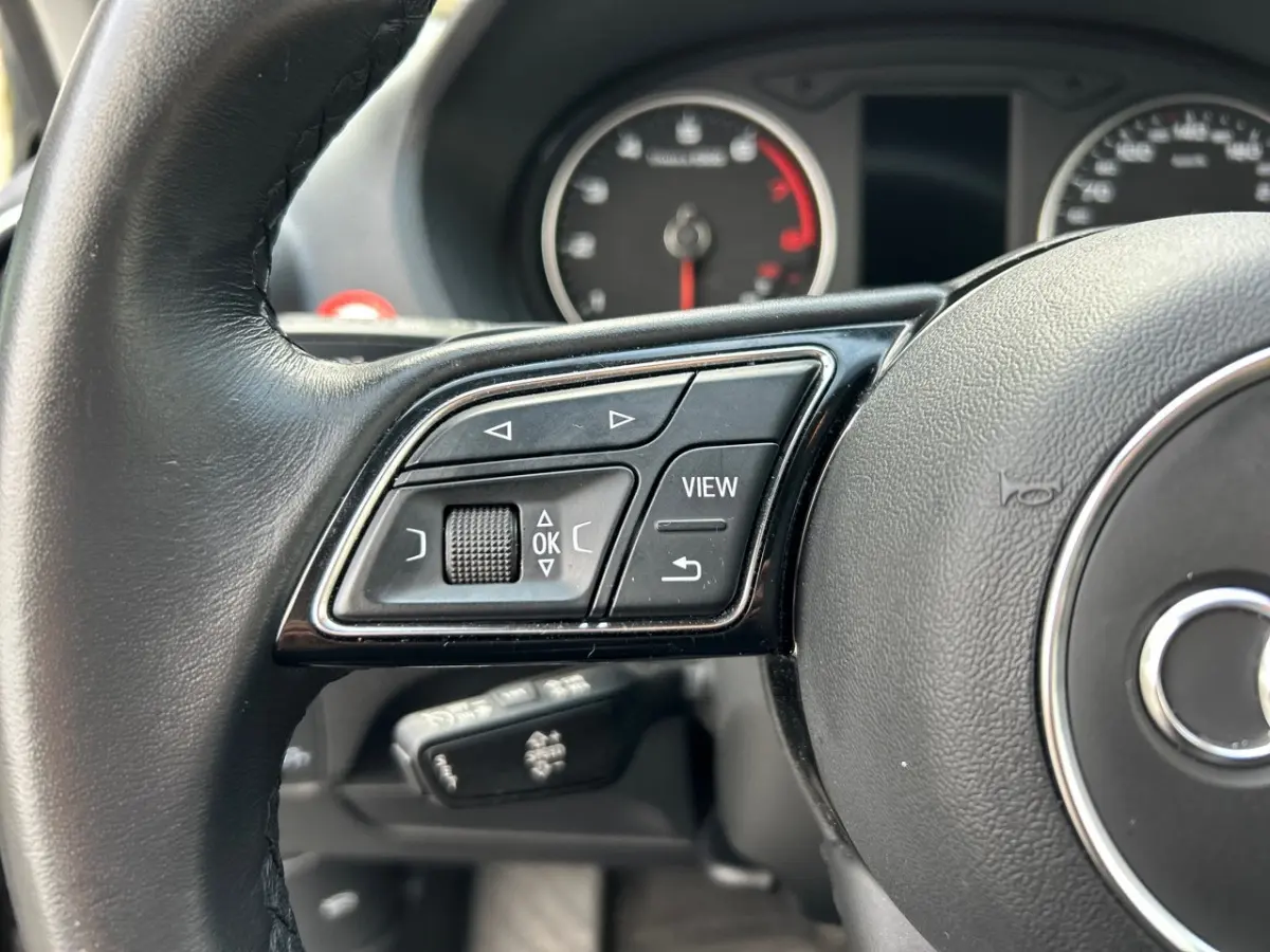 Gros plan sur les commandes du volant côté gauche de l'Audi Q2 35 TFSI 150 S Line 2023 avec cuir noir.