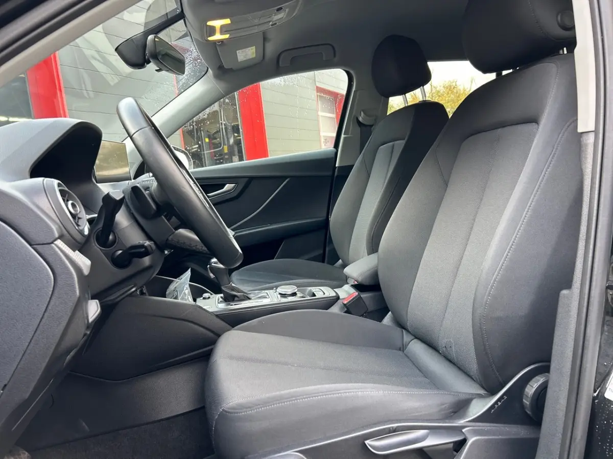 Intérieur de l'Audi Q2 35 TFSI 2023 vu côté conducteur, sièges tissu gris et volant multifonction cuir.