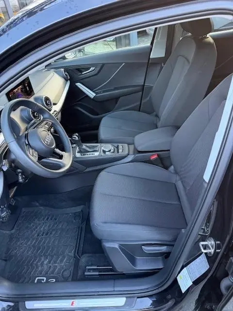 Intérieur noir de l'Audi Q2 35 TFSI 2023 vu côté conducteur, avec tableau de bord et sièges tissu gris.