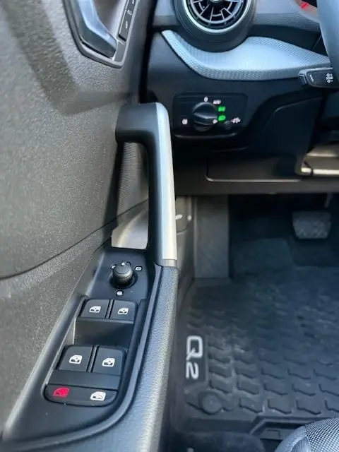 Gros plan sur la commande des vitres et rétroviseurs côté gauche d’un Audi Q2 noir, avec tapis de sol marqué Q2 visible.