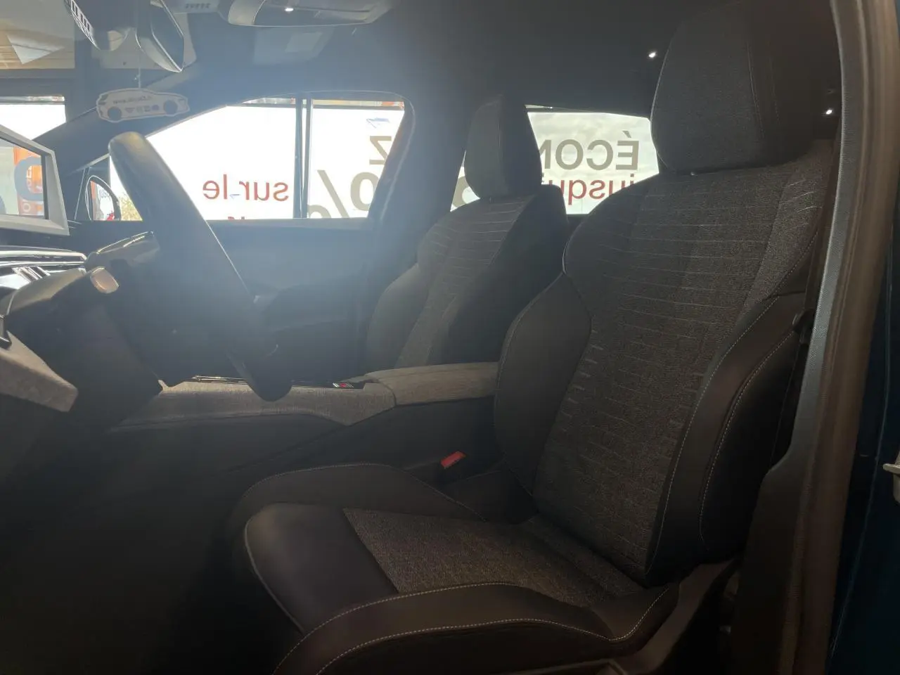 Vue intérieure côté conducteur du Peugeot 5008 bleu Obsession, sièges tissu gris et cuir noir avec surpiqûres contrastées.