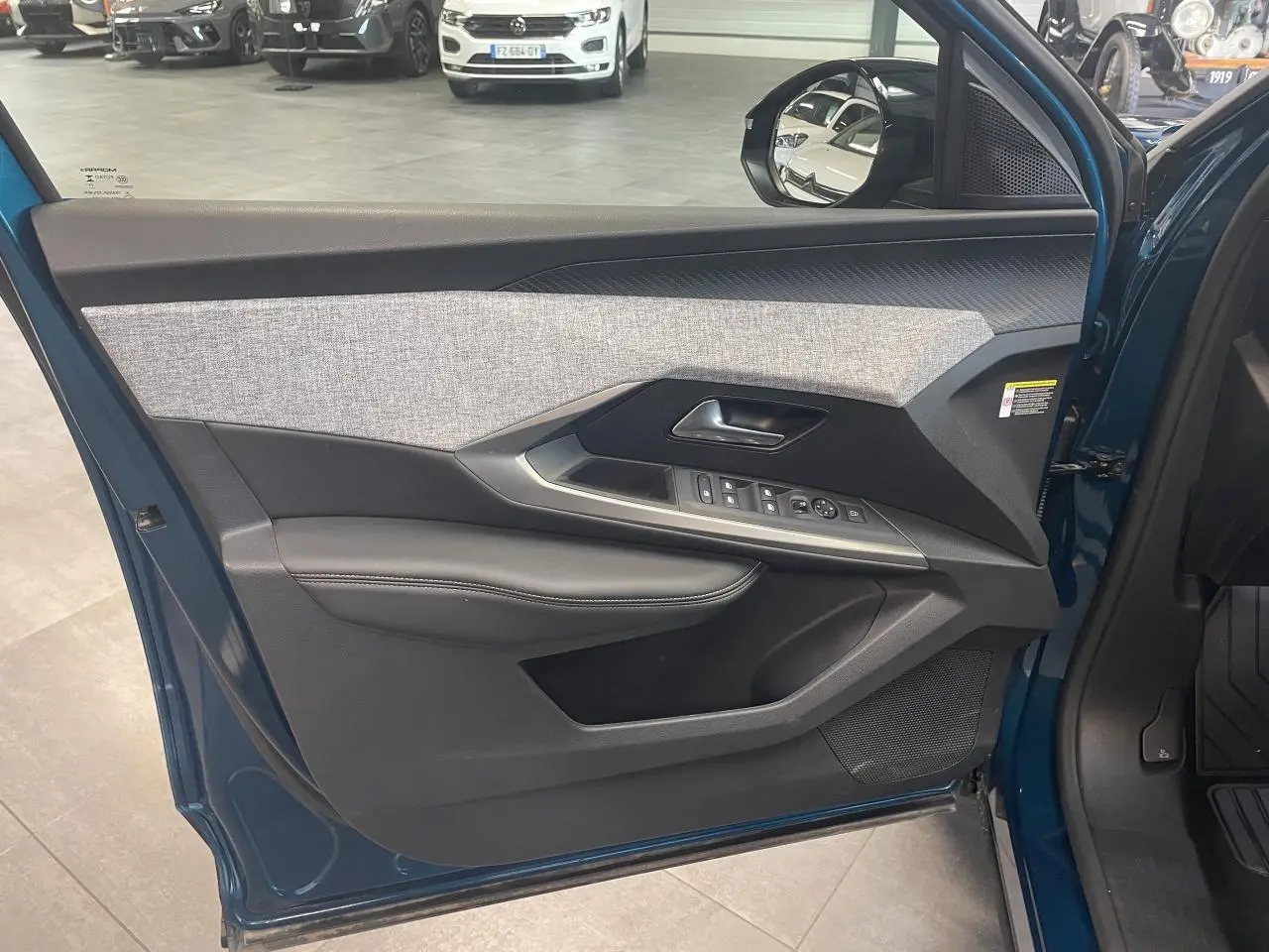 Vue intérieure de la porte avant gauche du Peugeot 5008 Bleu Obsession avec habillage tissu et commandes électriques.