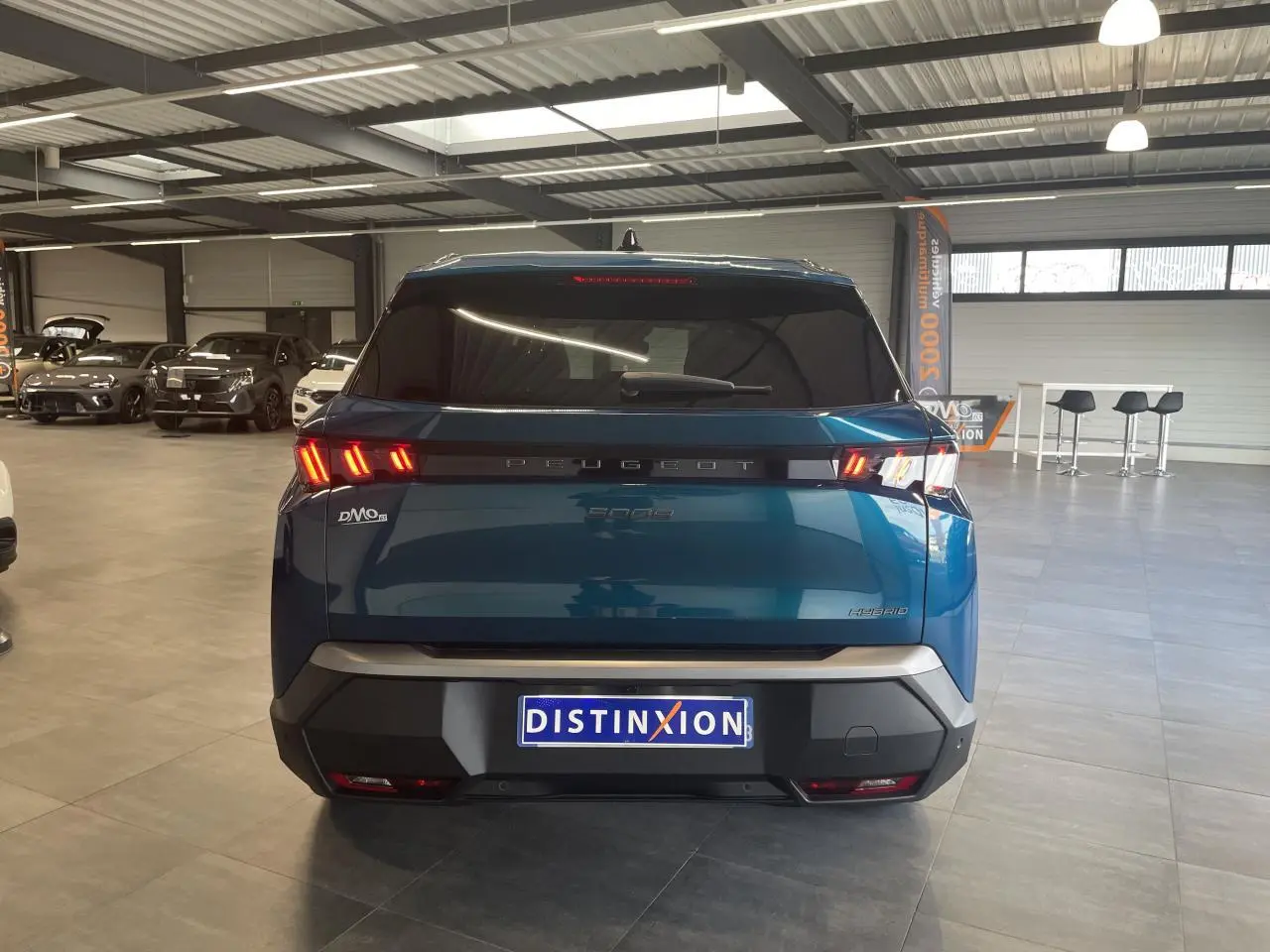 Vue arrière d’un Peugeot 5008 Bleu Obsession avec feux arrière LED 3 griffes et bandeau noir laqué en showroom.