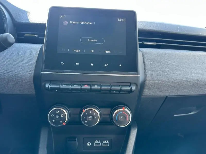 Vue frontale du tableau de bord gris clair de la Renault Clio 2025 avec écran tactile et commandes manuelles de climatisation.