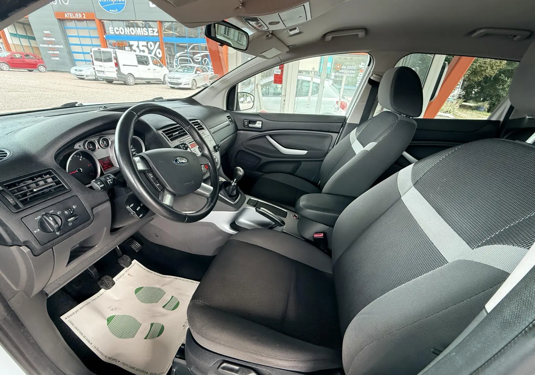 Intérieur avant du Ford Kuga blanc 2012, vue côté conducteur montrant tableau de bord et sièges tissu gris noir.