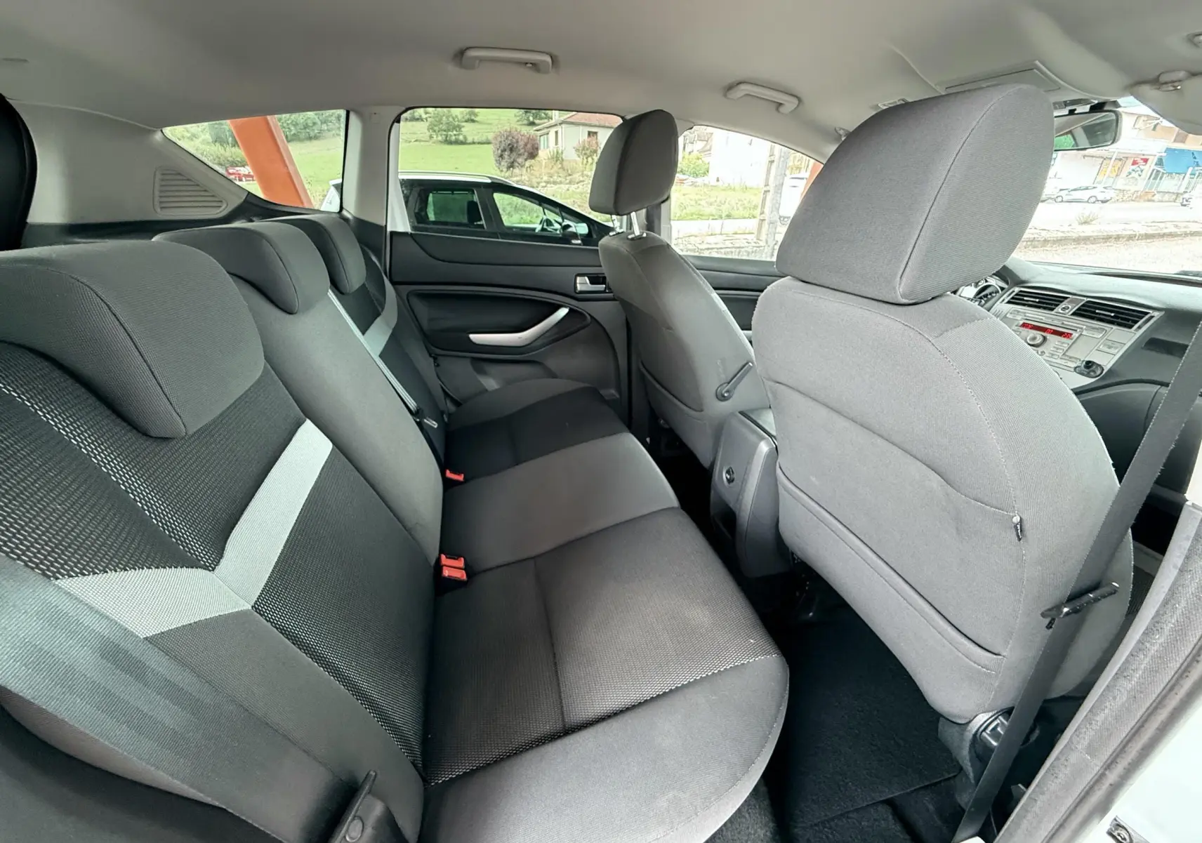 Vue intérieure arrière du Ford Kuga 2012 montrant les sièges en tissu gris et noir avec porte ouverte côté droit.