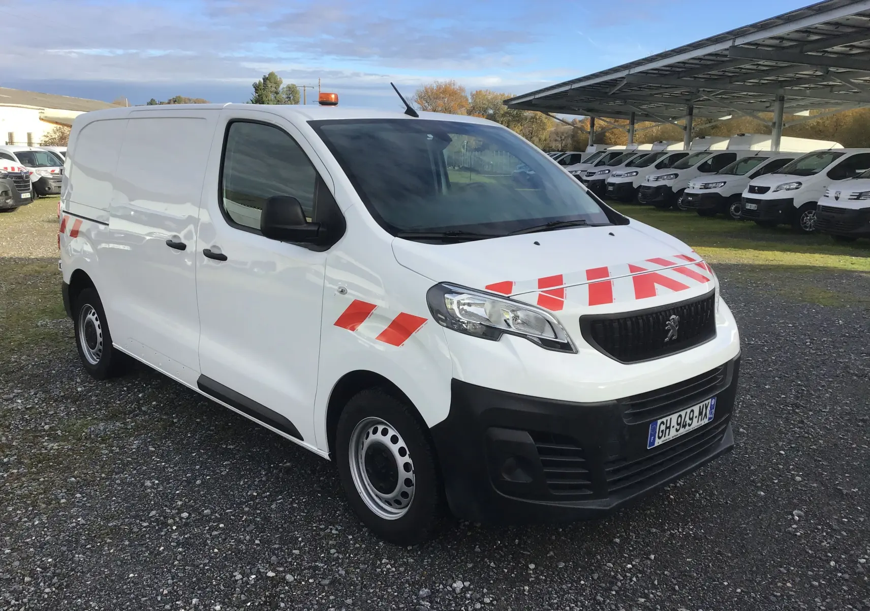 Vue 3/4 avant droit d'un Peugeot Expert Fourgon blanc 2022 avec bandes rouges et gyrophare orange sur le toit.