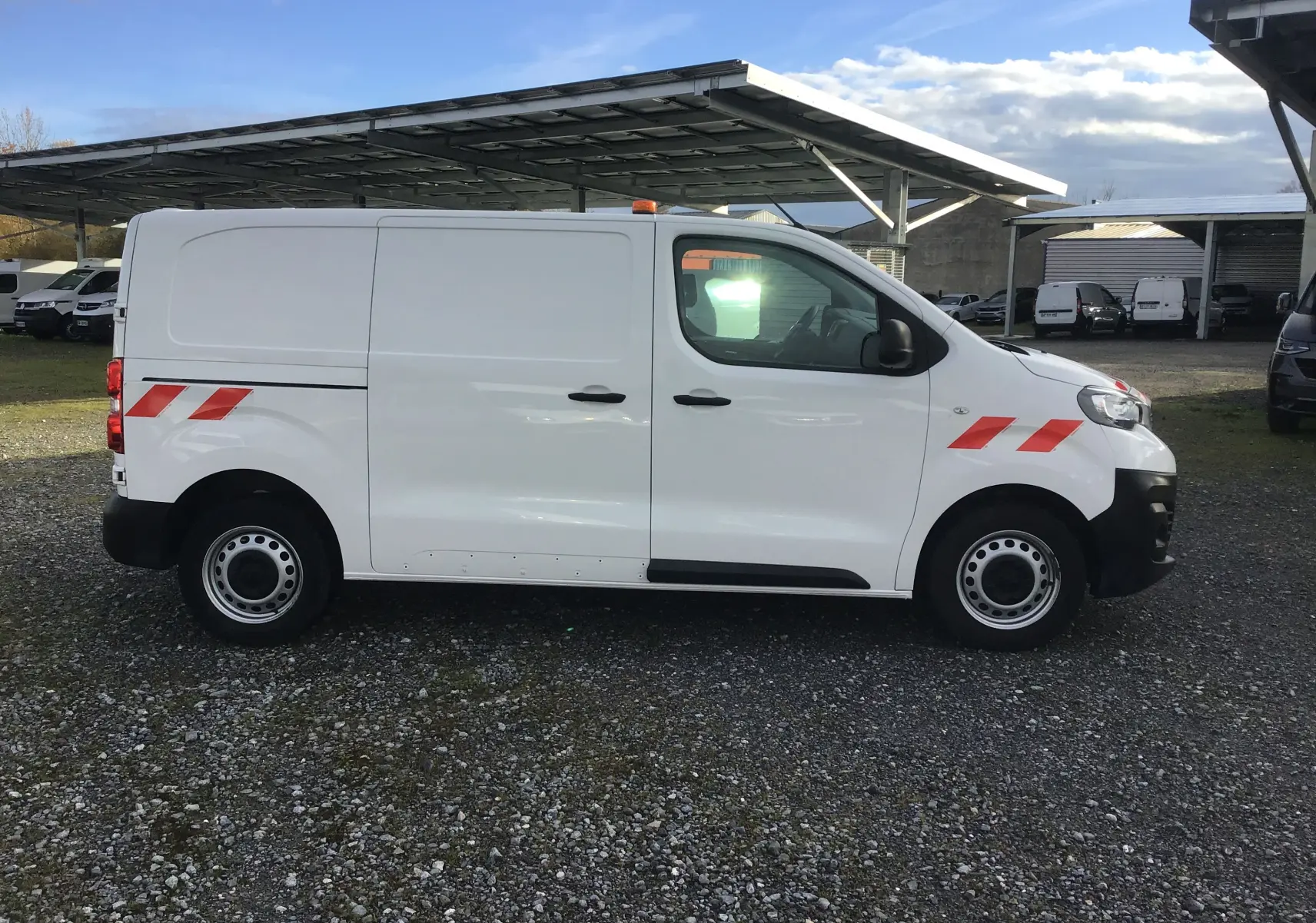 Vue 3/4 arrière d'un Peugeot Expert Fourgon blanc 2022 avec bandes réfléchissantes rouges et gyrophare.