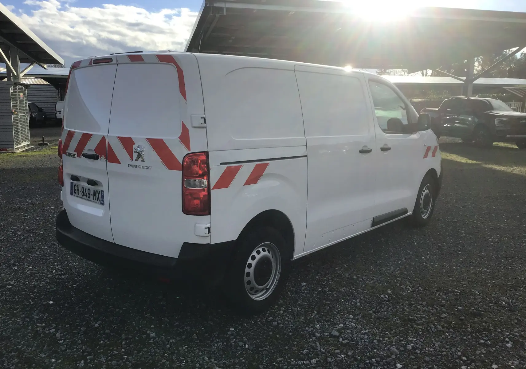 Vue arrière droite d'un Peugeot Expert Fourgon blanc 2022 avec bandes rouges réfléchissantes et gyrophare au toit.
