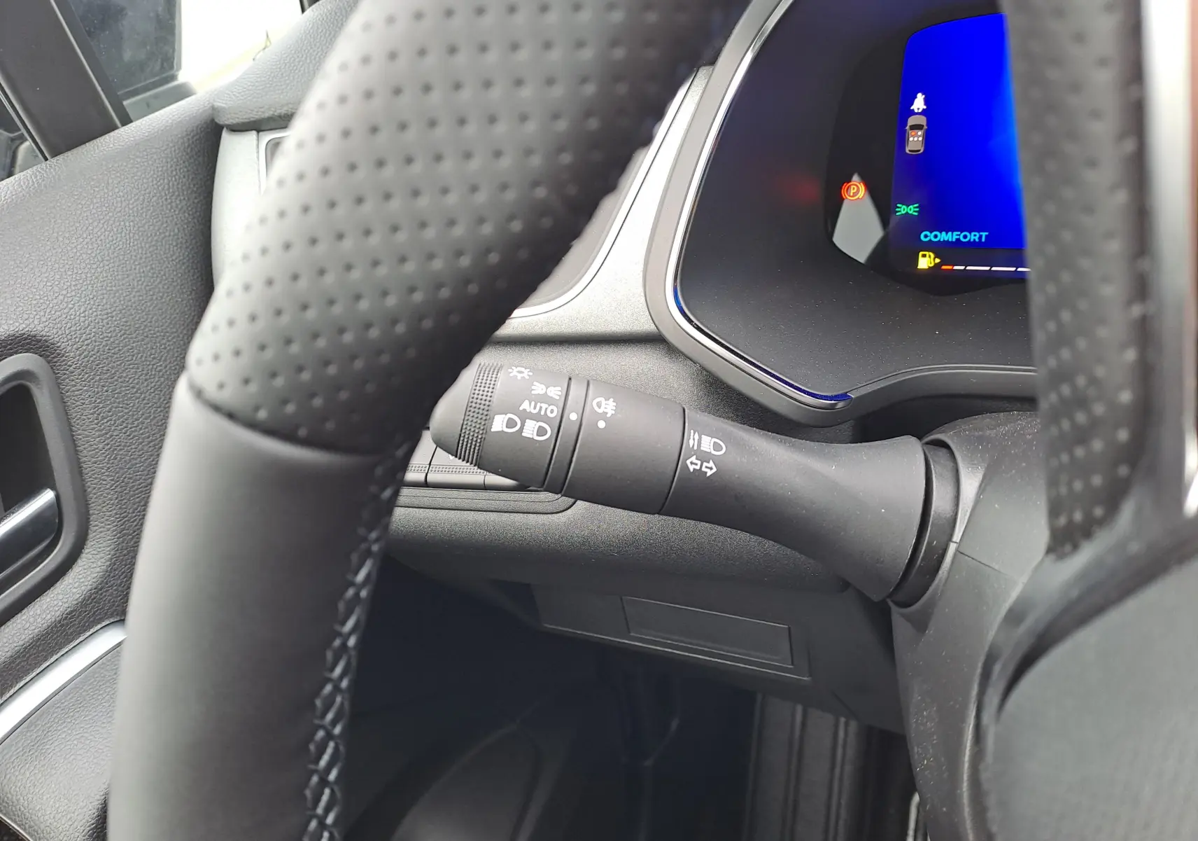 Gros plan intérieur sur le volant noir perforé et la commande des feux du Renault Symbioz 2025, avec tableau de bord digital bleu.