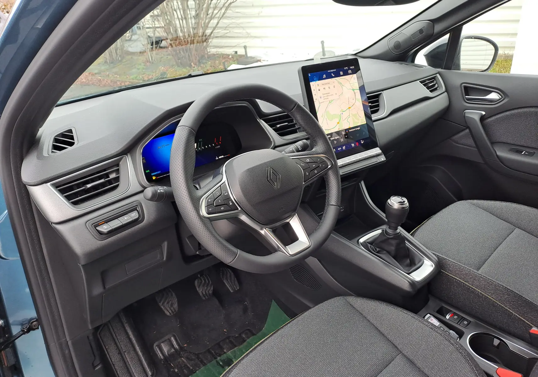 Vue intérieure côté conducteur de la Renault SYMBIOZ bleu mercure, avec volant multifonction et écran tactile vertical.