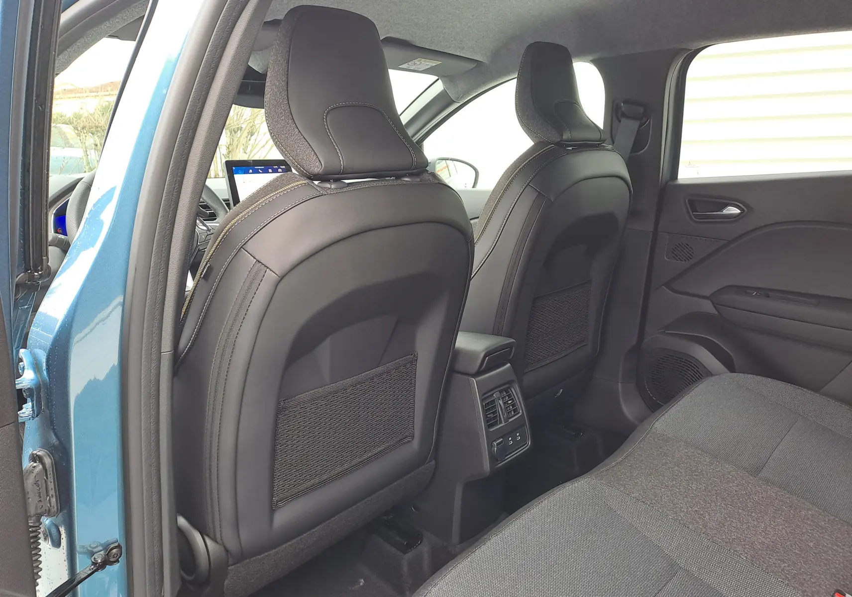 Vue arrière intérieure de la Renault Symbioz bleu mercure, montrant les sièges avant en cuir noir et la banquette arrière tissu gris.