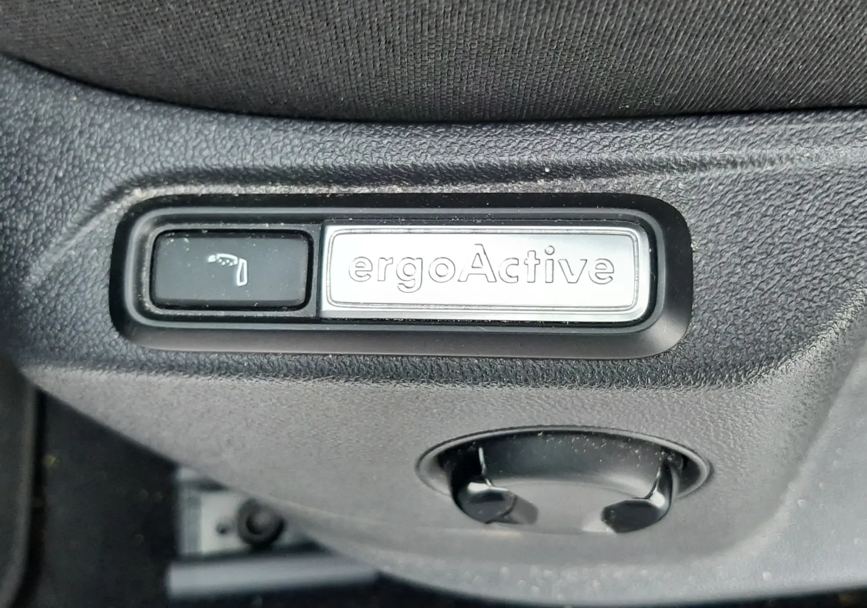 Gros plan sur la commande ergoActive du siège côté conducteur dans l'habitacle du Volkswagen T-Roc gris pyrite.