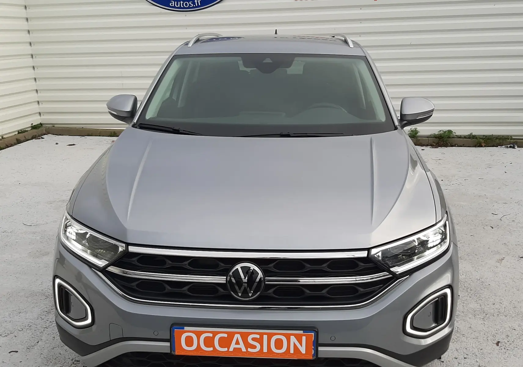 Vue frontale d'un Volkswagen T-Roc gris pyrite 2023 avec calandre noire et feux LED allumés.