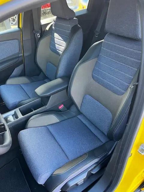 Vue intérieure côté avant droit de la Renault R5 jaune 2024, sièges en tissu bleu avec accoudoir central.