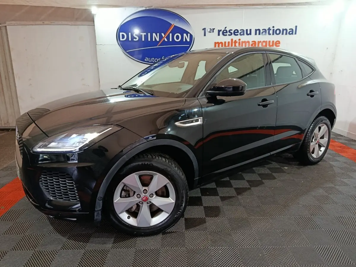 Jaguar E-PACE noir en 3/4 avant droit, avec jantes argentées et phares LED allumés en intérieur showroom.