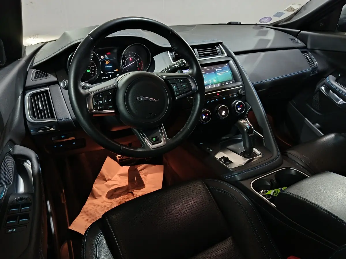 Vue intérieure côté conducteur du Jaguar E-PACE noir, volant cuir multifonctions et écran tactile central visible.