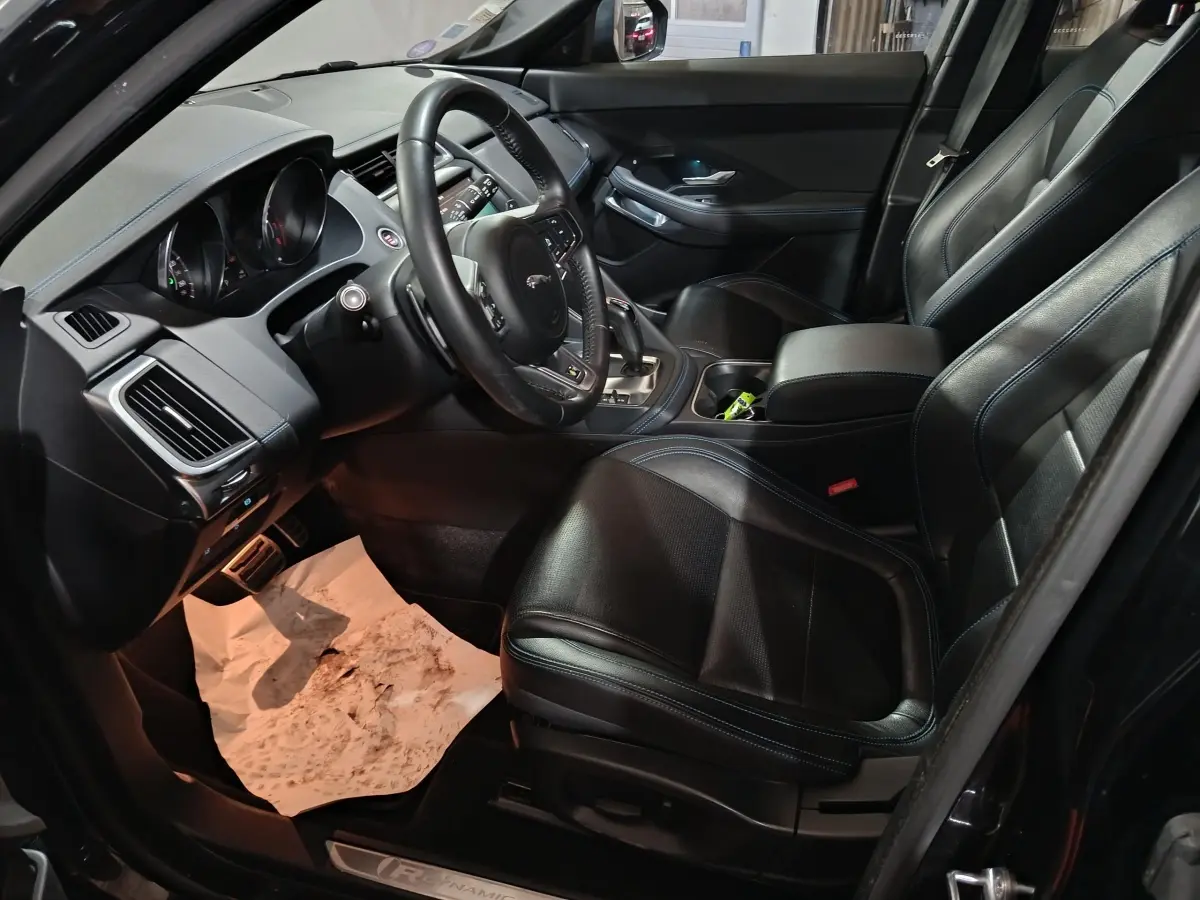 Vue intérieure côté conducteur du Jaguar E-PACE noir, mettant en valeur le volant cuir multifonctions et les sièges sport noirs.