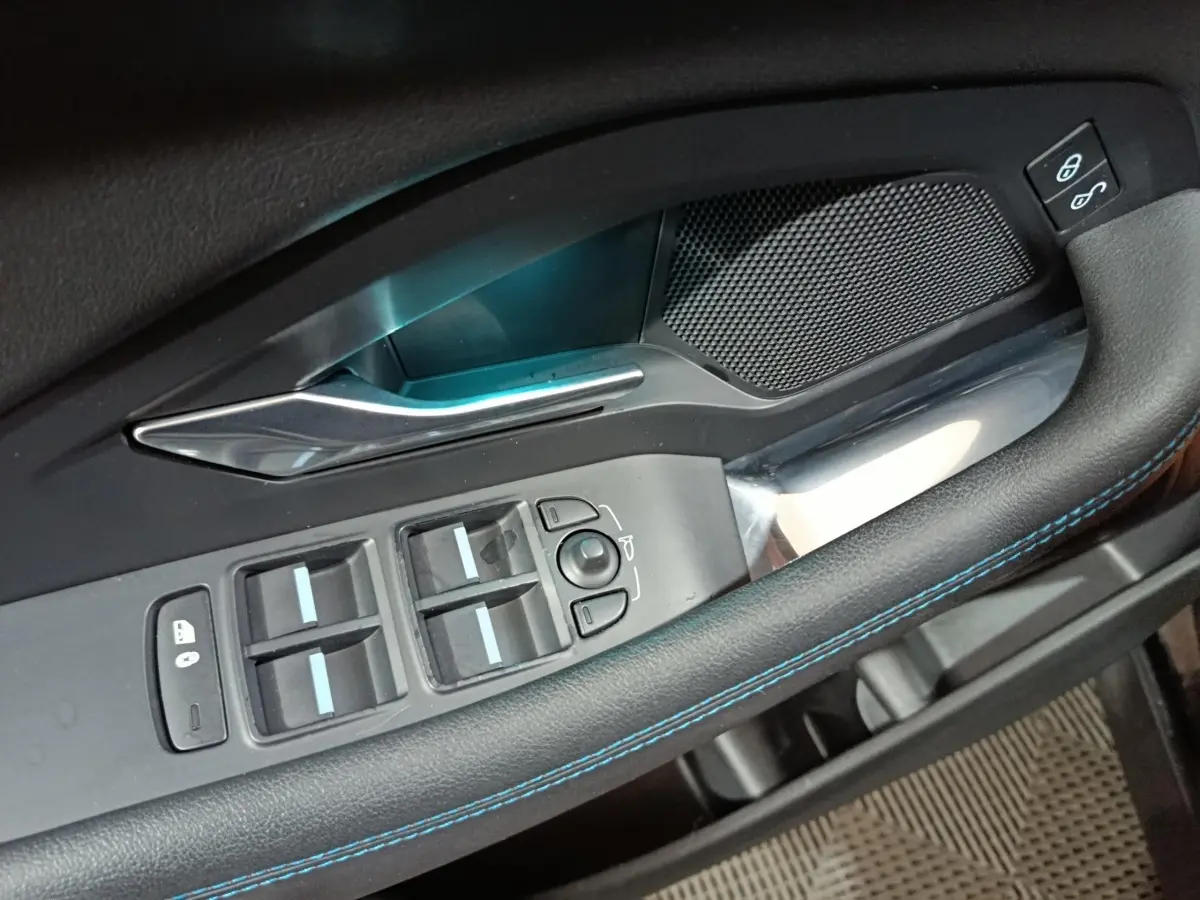 Gros plan sur la commande des vitres côté conducteur du Jaguar E-PACE noir, avec surpiqûres bleues et poignée argentée.