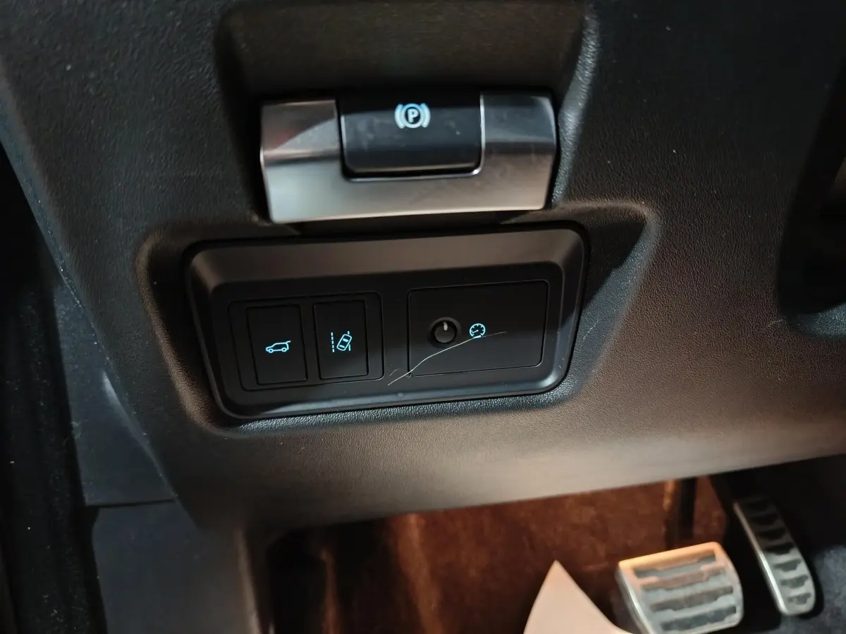 Gros plan sur les commandes sous le volant noir du Jaguar E-PACE P200, avec bouton frein à main électrique et régulateur de vitesse.