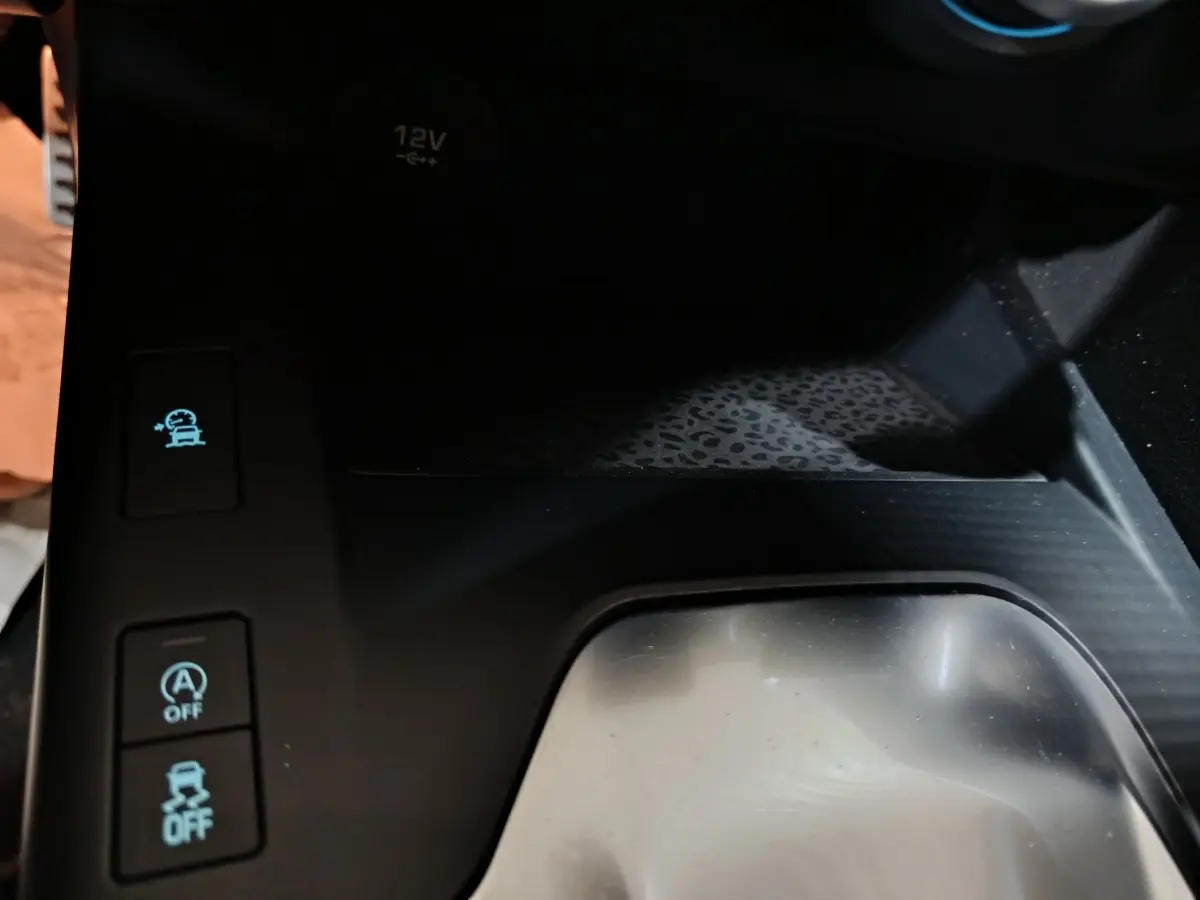 Gros plan sur la console centrale noire du Jaguar E-PACE 2019, avec boutons d’aide à la conduite et prise 12V visible.