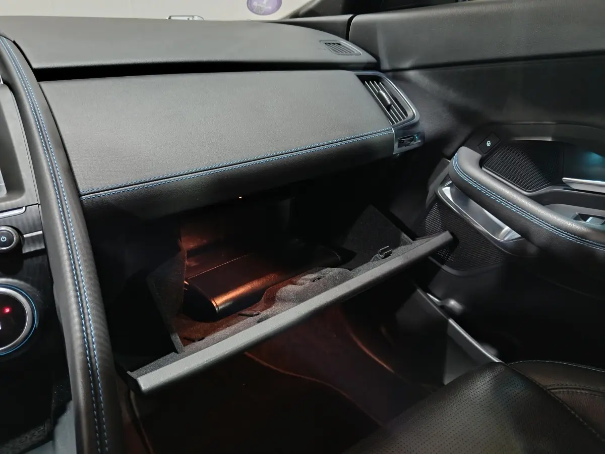 Intérieur noir du Jaguar E-PACE 2019, vue côté passager avec boîte à gants ouverte et surpiqûres bleues.