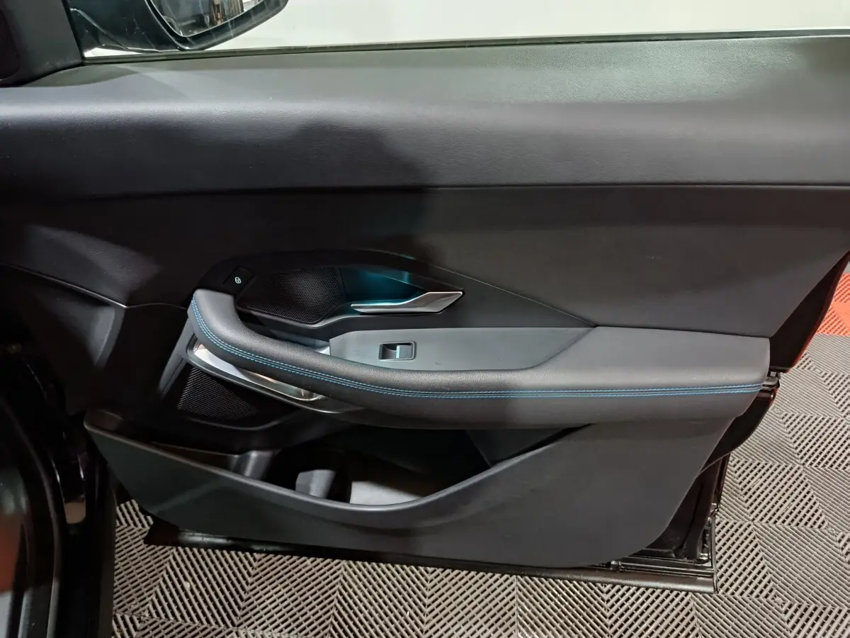 Vue latérale du panneau de porte intérieur noir de la Jaguar E-PACE 2019 avec surpiqûres bleues et poignée argentée.
