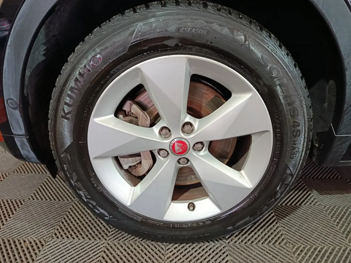 Gros plan sur la roue avant gauche d'une Jaguar E-PACE noire, avec jante argentée et logo Jaguar rouge au centre.