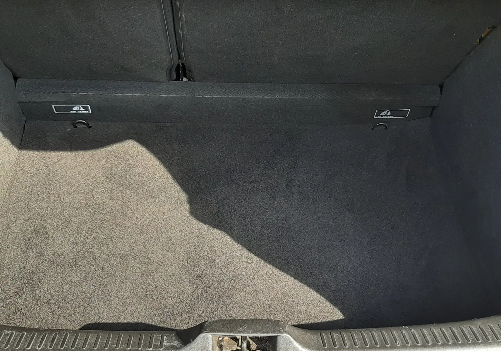 Coffre ouvert vu de dessus, intérieur noir propre avec tapis de sol et crochets de fixation visibles.