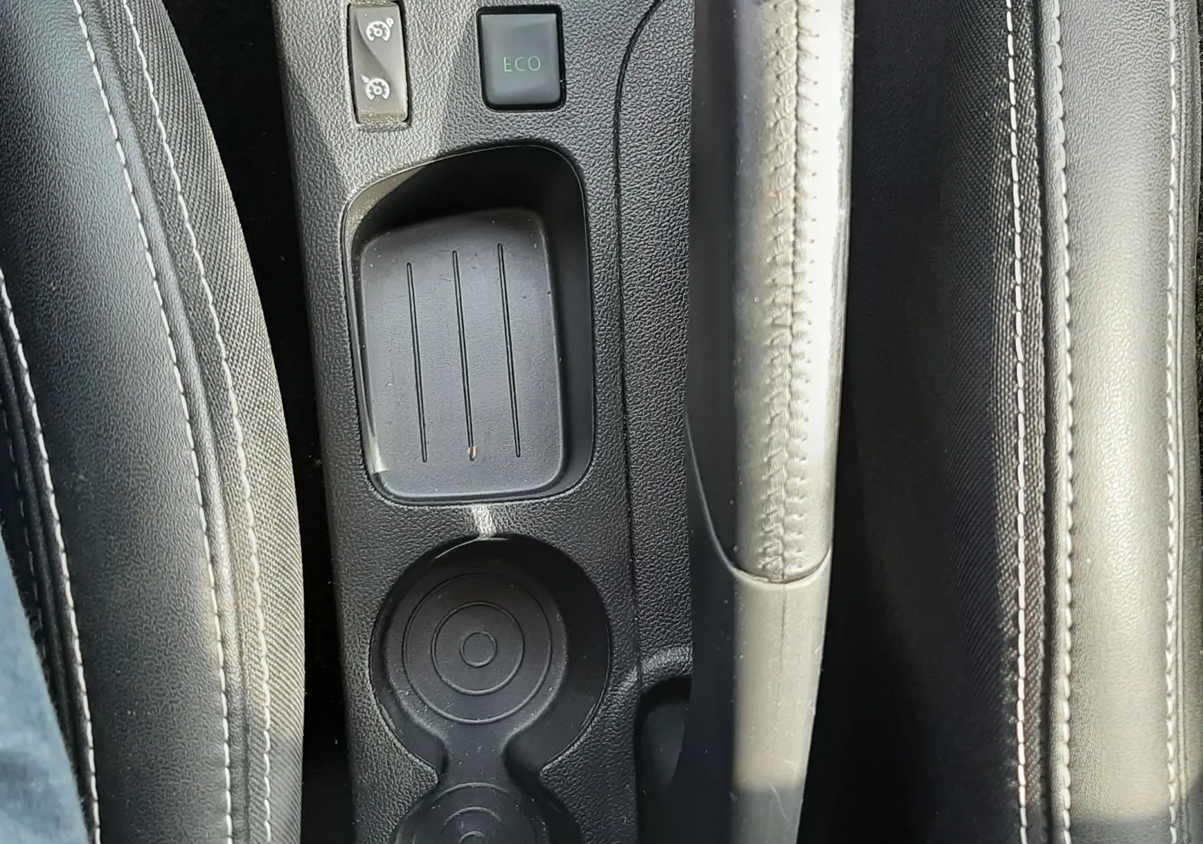 Vue plongeante sur la console centrale noire de la Renault Clio IV avec frein à main, bouton ECO et porte-gobelets.