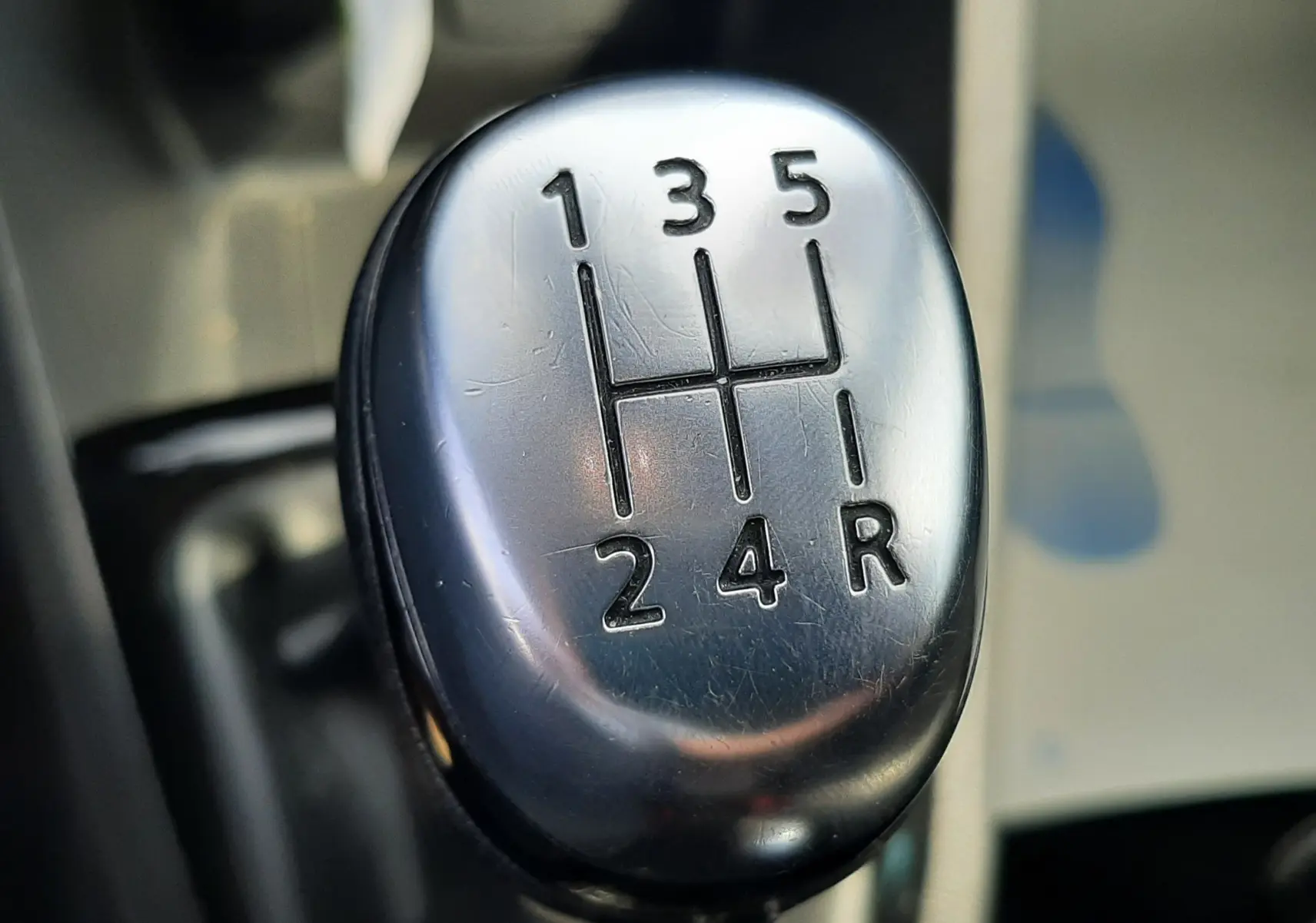 Gros plan sur le levier de vitesse manuel argenté de la Renault Clio IV noire, montrant les rapports 1 à 5 et la marche arrière.