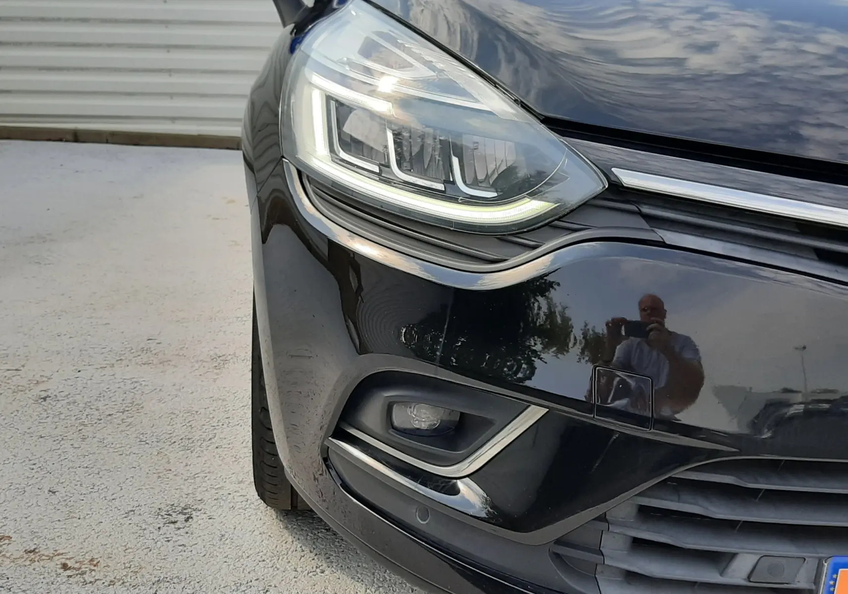 Gros plan sur l'avant gauche noir brillant d'une Renault Clio IV 2018, mettant en valeur son phare LED et le pare-chocs.