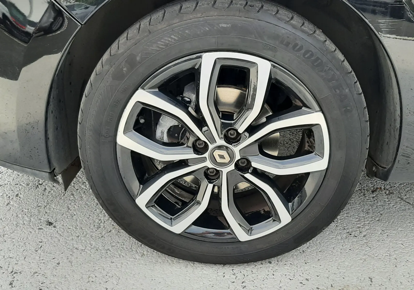 Gros plan sur la roue avant gauche d'une Renault Clio IV noire, mettant en valeur la jante alliage bicolore au design moderne.