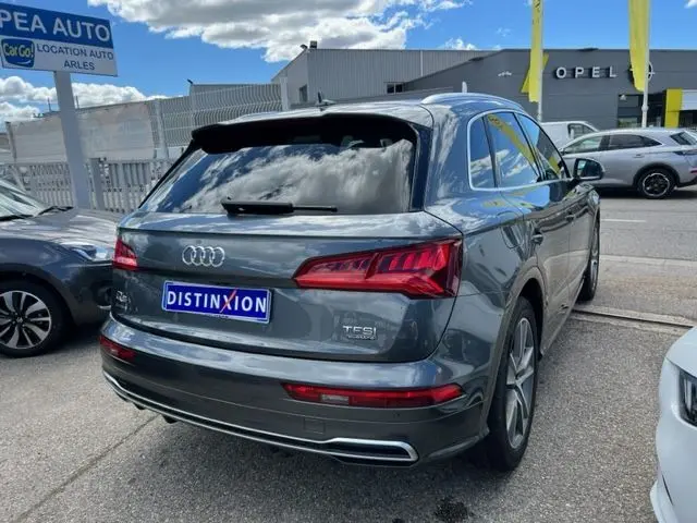 Audi Q5 gris foncé vue 3/4 arrière droit, finition S Line avec feux LED et double sortie d'échappement intégrée.