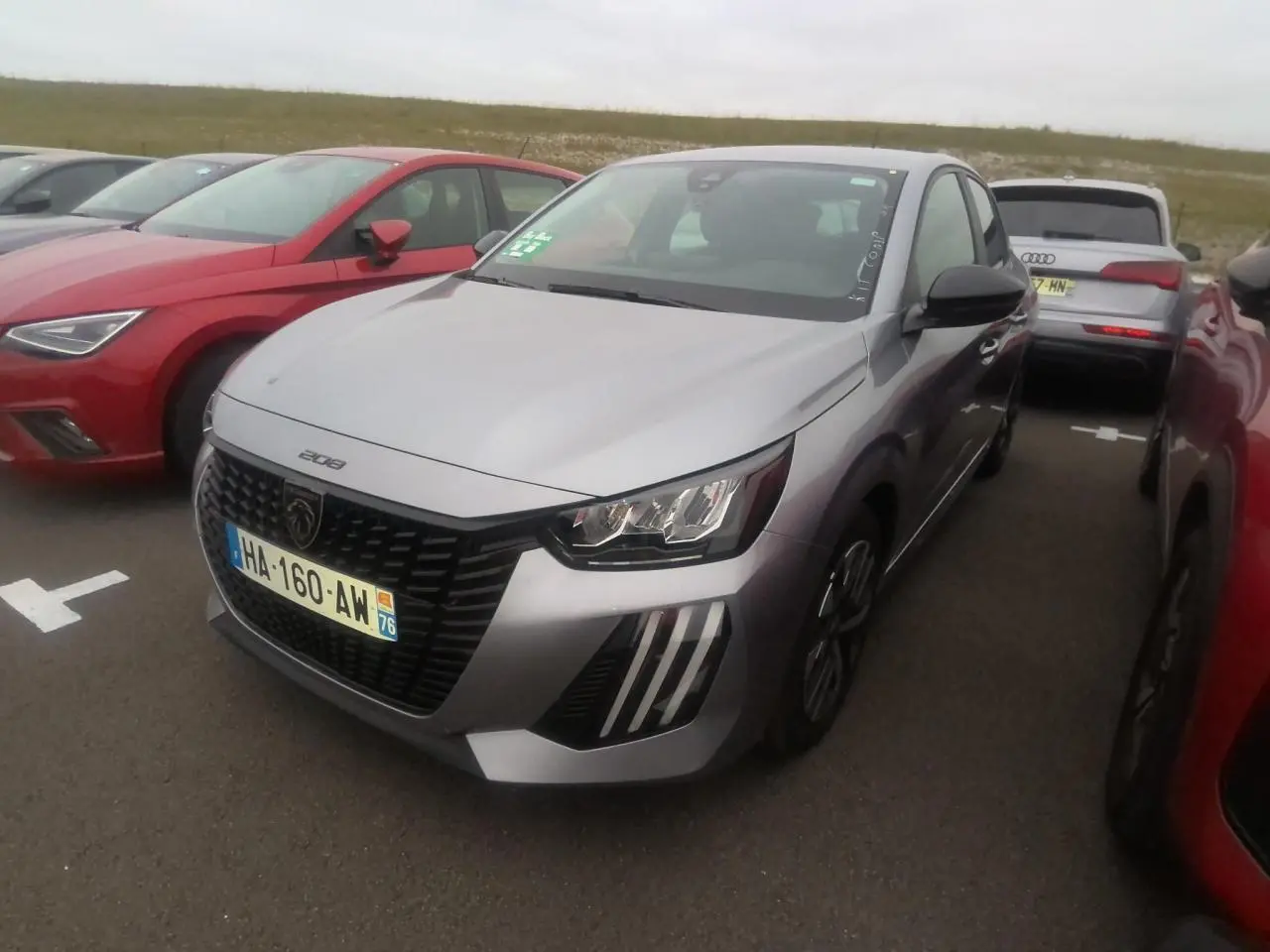 Peugeot 208 gris clair vue 3/4 avant droit avec calandre noire et feux à signature LED 3 griffes.